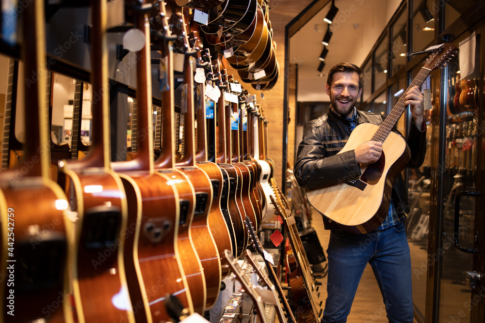 Talented caucasian musician in leather jacket checking and testing new guitar instrument he wants to buy in music shop.