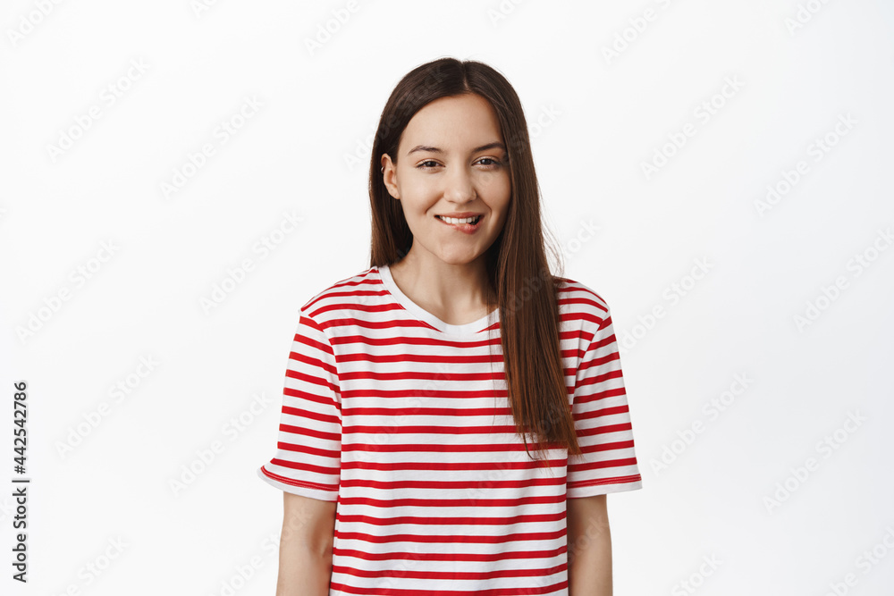 Girl looks at smth tasty. Smiling cute woman biting lip and squinting from tempation, want to try delicious thing, tempted with something, standing in striped t-shirt against white background Girl looks at smth tasty. Smiling cute woman biting lip and squinting from tempation, want to try delicious thing, tempted with something, standing in striped t-shirt against white background