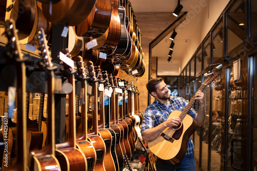 Talented caucasian musician checking the sound of new guitar instrument in music shop.