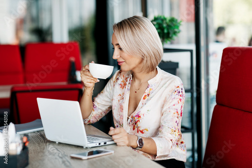 An elegant business woman drinks coffee, works in a cafe, uses a laptop, enjoys a break. Business, online business, freelance