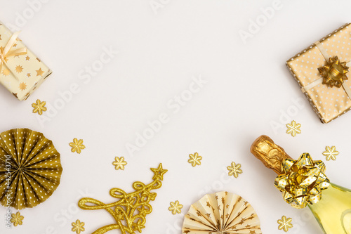 Festive background with gold decoration , gift boxes with bottle of sparkling wine, shiny golden serpentine confetti and paper Christmas tree decorations, glittering snowflakes and Christmas tree