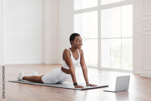 Young african woman stretching back on mat with pc