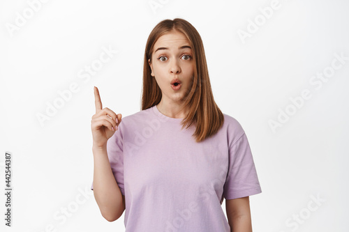 Got excellent idea. Excited blond girl says suggestion, pointing up and gasp thrilled, showing announcement, event advertisement or store banner, standing over white background