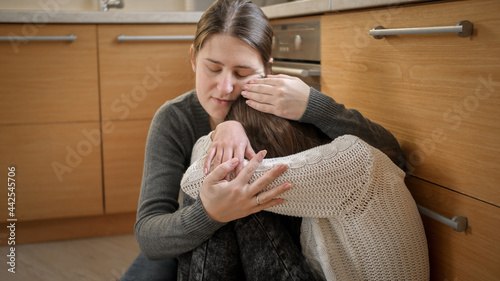 Slika na platnu Young mother sitting next to crying daughter and comforting her