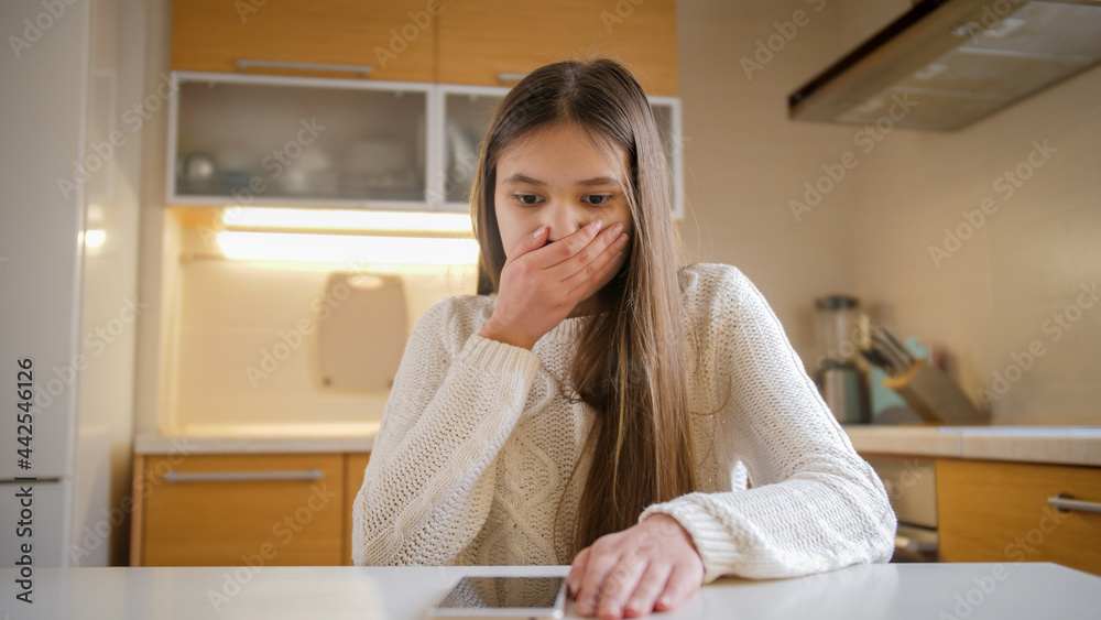Teenage girl got shocked closing her moth with hands after reading bad news or receiving negative message on smartphone Teenage girl got shocked closing her moth with hands after reading bad news or receiving negative message on smartphone