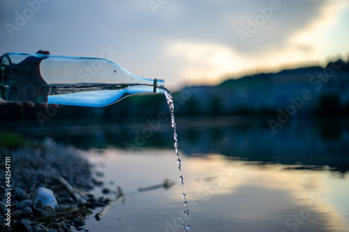 Glasflasche giesst Wasser in den Fluss
