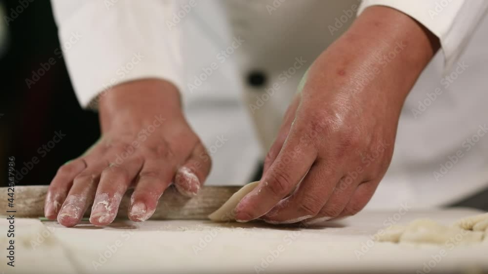 Rolling the round edge of a dumpling with a wooden pin - side view chef in traditional uniform Rolling the round edge of a dumpling with a wooden pin - side view chef in traditional uniform