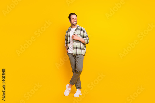 Full length photo of happy positive young man look empty space wear glasses isolated on yellow color background