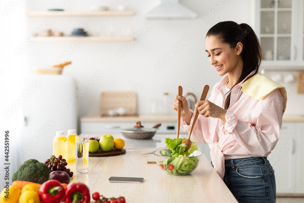 Portrait of smiling young woman cooking fresh salad in kitchen