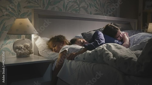 Young attractive mother reading book with fairy tales for children, daughters before sleeping in the bed. Woman and two girls getting ready for good night. Bed time together. Slow motion shot.