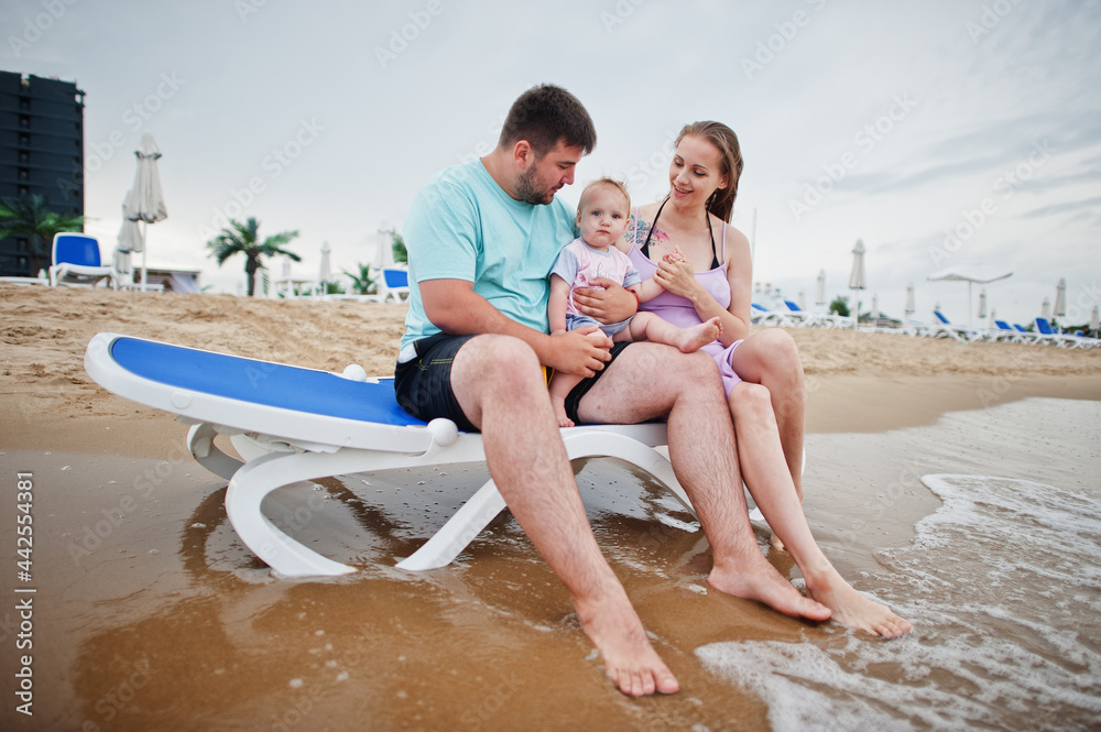 Fototapeta premium Summer vacations. Parents and people outdoor activity with children. Happy family holidays. Father, pregnant mother, baby daughter sitting on sunbed at sea sand beach.