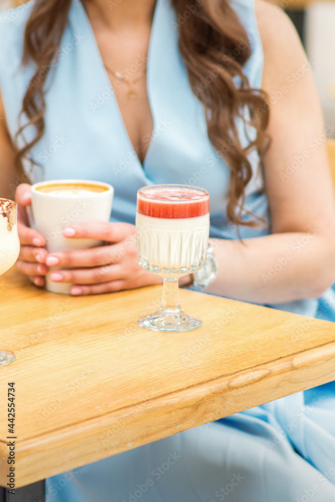 Hands of a young woman holding a cup of coffee with different cocktails on the table at the cafe. Hands of a young woman holding a cup of coffee with different cocktails on the table at the cafe.