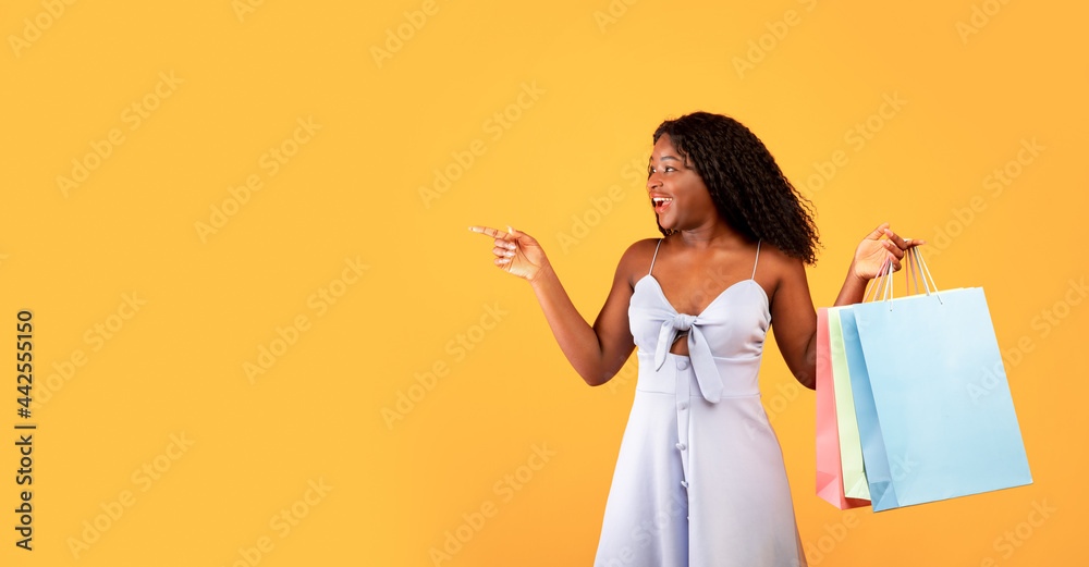 Excited young black woman with shopping bags pointing aside, offering big sale or unexpected promo on orange background Excited young black woman with shopping bags pointing aside, offering big sale or unexpected promo on orange background