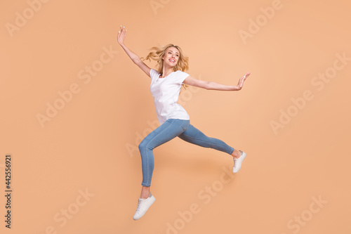 Photo of pretty sweet young woman dressed white t-shirt jumping high walking smiling isolated beige color background