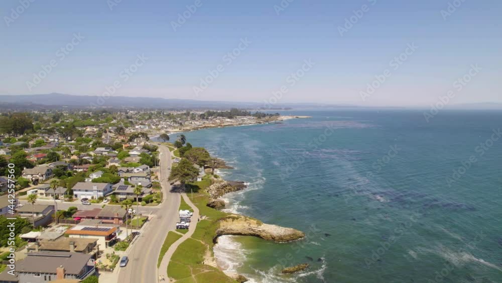 Long shot of drone flying along the cliffs of the small coastal town of Santa Cruz, CA. Cars driving along the ocean and people exersizing near the sea with aerial views of waves and cliffs in nature. Long shot of drone flying along the cliffs of the small coastal town of Santa Cruz, CA. Cars driving along the ocean and people exersizing near the sea with aerial views of waves and cliffs in nature.