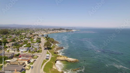 Long shot of drone flying along the cliffs of the small coastal town of Santa Cruz, CA. Cars driving along the ocean and people exersizing near the sea with aerial views of waves and cliffs in nature.