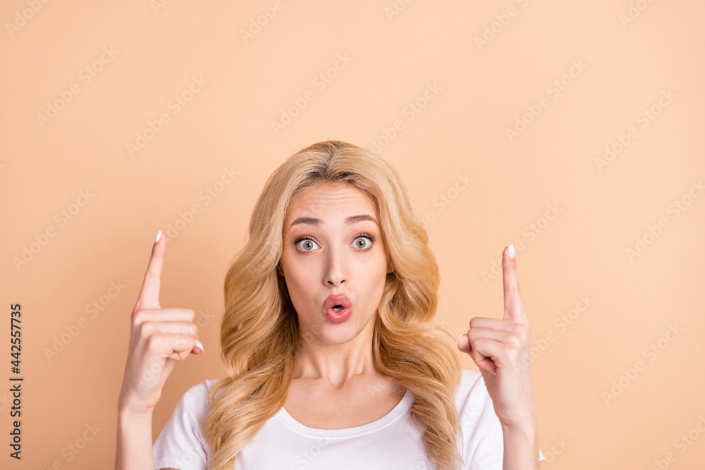 Photo of charming impressed young lady wear white t-shirt big eyes pointing up empty space isolated beige color background Photo of charming impressed young lady wear white t-shirt big eyes pointing up empty space isolated beige color background