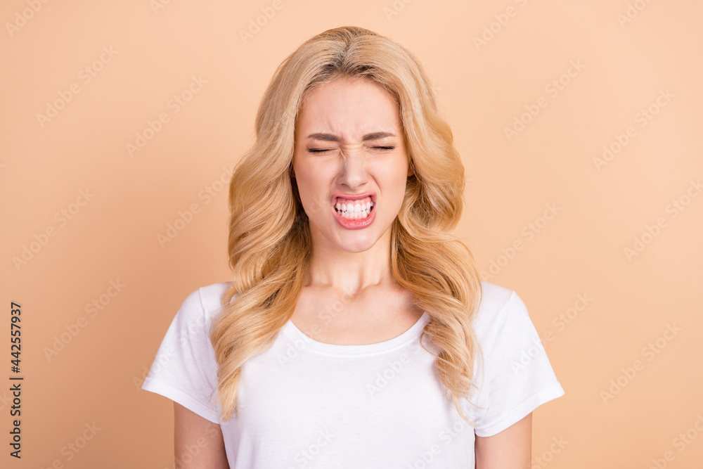 Photo of unhappy angry young woman dressed white t-shirt showing teeth closed eyes isolated beige color background Photo of unhappy angry young woman dressed white t-shirt showing teeth closed eyes isolated beige color background