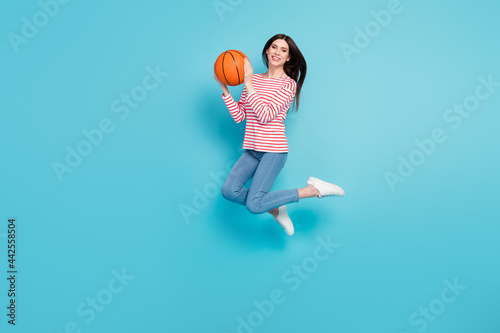 Full length body size view of attractive cheerful girl jumping holding basket ball isolated over bright blue color background
