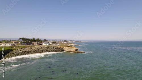 California coastline with epic views of the ocean and water with people living by the water. Waves crashing along coastal cliff edges with long drone shots and houses in a small town. 