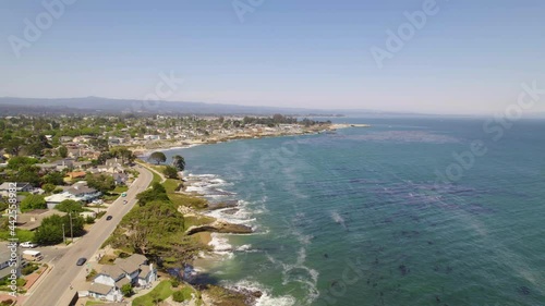 California coastline with epic views of the ocean and water with people living by the water. Waves crashing along coastal cliff edges with long drone shots and houses in a small town. 