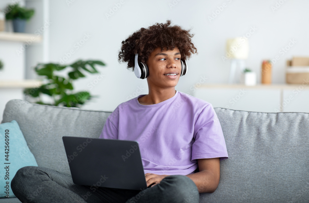 Distance education. Black teenager in headphones having online conference or remote lesson on laptop at home Distance education. Black teenager in headphones having online conference or remote lesson on laptop at home