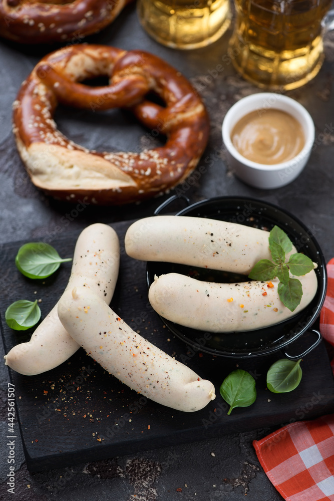 Weisswurst or german white sausages on a black wooden serving board and pretzels, studio shot, selective focus