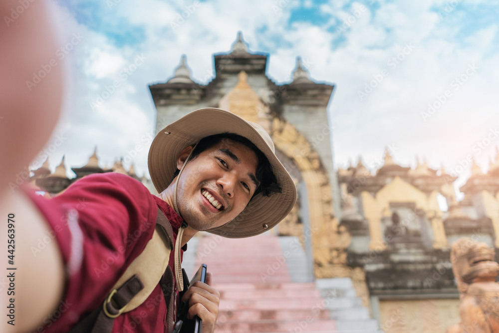 Asian man traveler wearing a hat smile selfie with architecture pagoda ancient of Asia. Tourism south east Asia culture. Backpacker happy travel south east Asia.