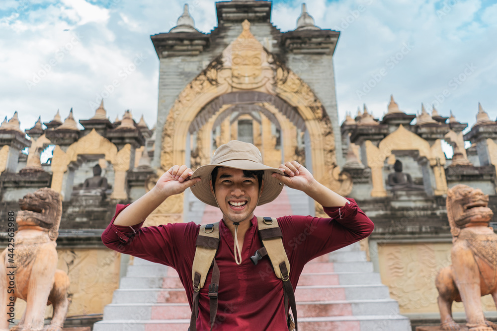 Portrait Asian man backpacker travel pagoda in southeast Asia. Happy traveler wearing a hat carrying a backpack on a Buddhist temple.