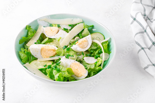 Salad with eggs, lettuce, cheese, cucumber, white radish and scallion served in the bowl on the white table