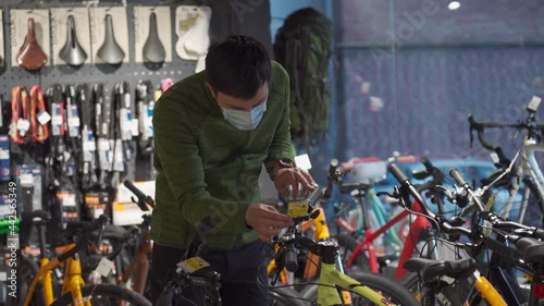 Masked man has no way of choosing bike at bicycle shop. Shopper wearing face shield at sports store selects cycle during COVID 19. Customer wearing mask in velocipede shop buying bicycle. photo