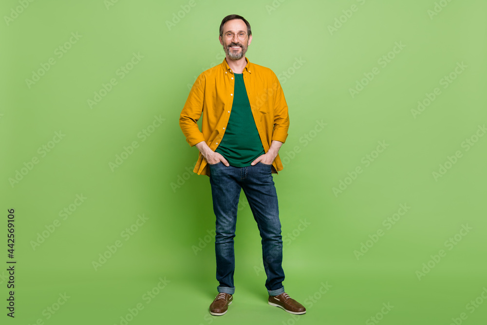 Full length photo of mature business man happy positive smile hands in pocket chief isolated over green color background Full length photo of mature business man happy positive smile hands in pocket chief isolated over green color background