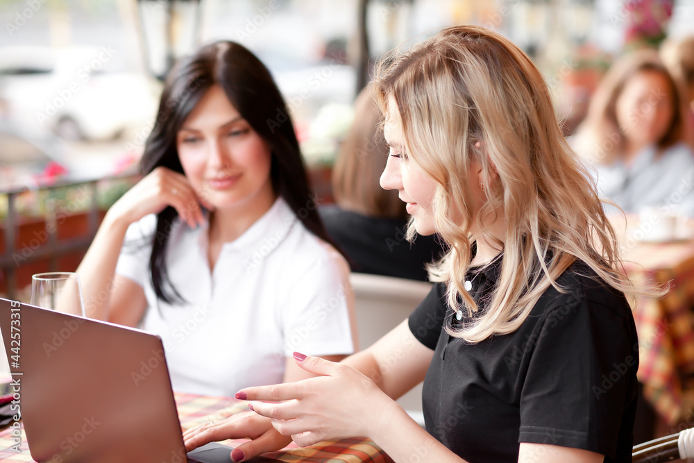 Beautiful women workers or students using laptop at cafe and talking Beautiful women workers or students using laptop at cafe and talking