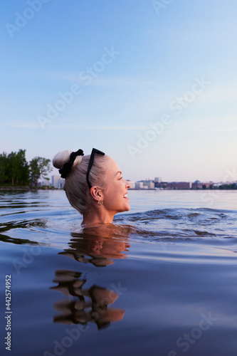 A beautiful blond woman swimming in sea in helsinki during evening twilight sunlight sunset in nordic in finland Kalasatama in background