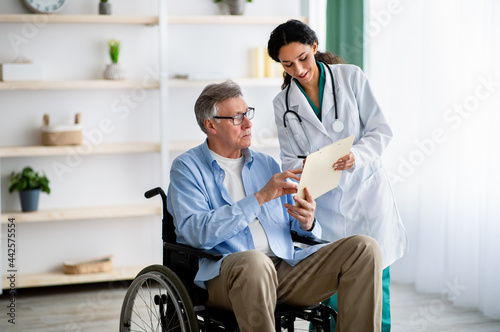 Fotografie Young nurse offering handicapped elderly man in wheelchair to sign insurance con