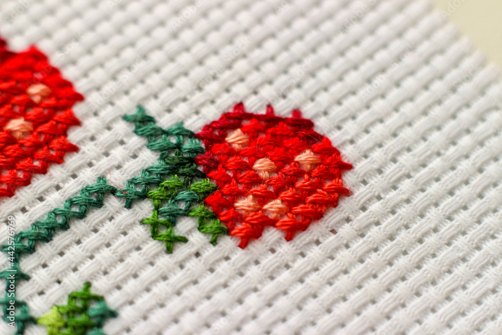Red ripe strawberries embroidered with a cross-stich on a white canvas by hand. Close up, macro.