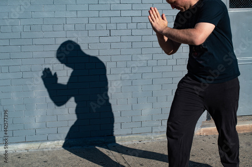 Man shadow cast on a wall in a bright light, street setting.