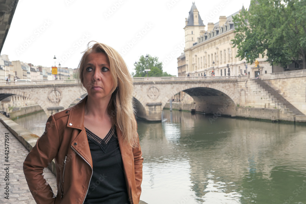 Portrait of a mature blonde woman in the city of Paris. Saint Michel bridge and Seine river blurred deliberately in the background.