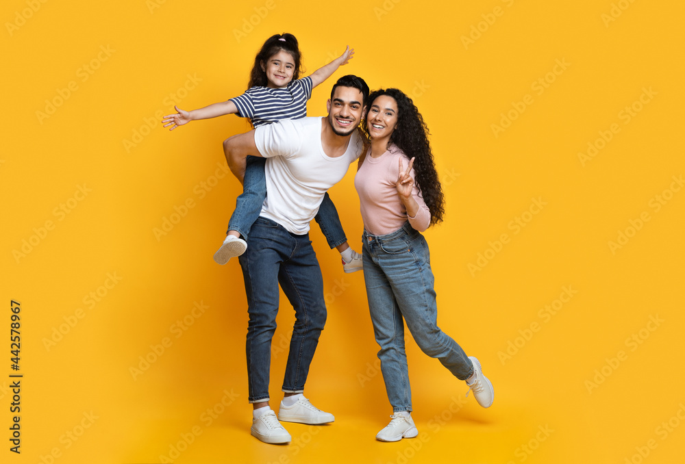 Cheerful Middle Eastern Family Of Three Having Fun Together Over Yellow Background