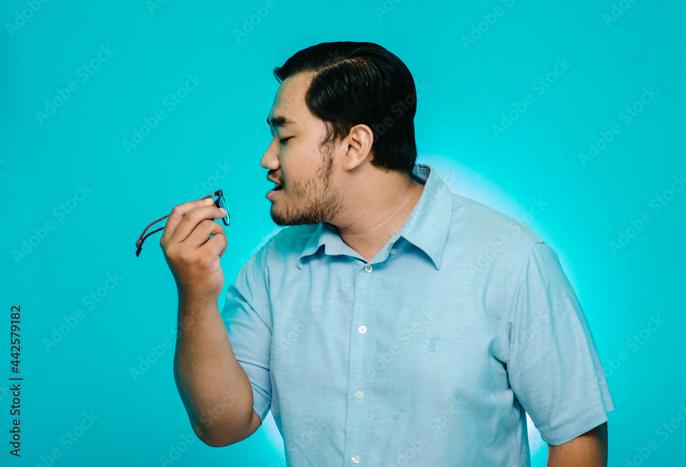 Young man blowing glasses in hand on blue background Young man blowing glasses in hand on blue background