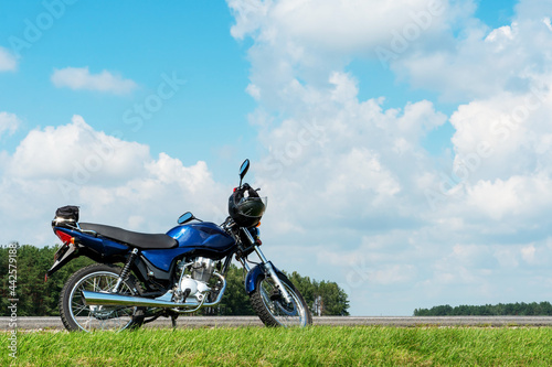 Fototapeta Naklejka Na Ścianę i Meble -  A motorcycle trip through the countryside in the summer. A blue motorcycle on a background of blue sky and white clouds.