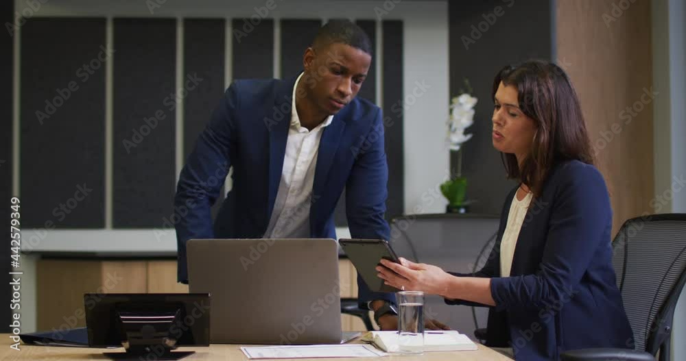 Diverse businessman and businesswoman discussing and using laptop in modern office Diverse businessman and businesswoman discussing and using laptop in modern office