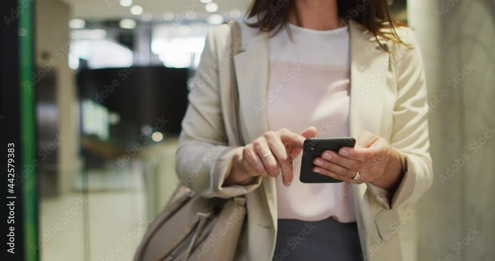 Caucasian businesswoman using smartphone in corridor of modern office Caucasian businesswoman using smartphone in corridor of modern office