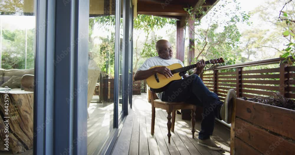 Thoughtful african american senior man sitting on balcony playing ...