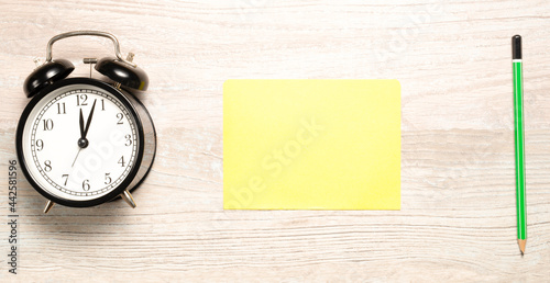 yellow card to write down a note with a clock and a green pencil on the desk