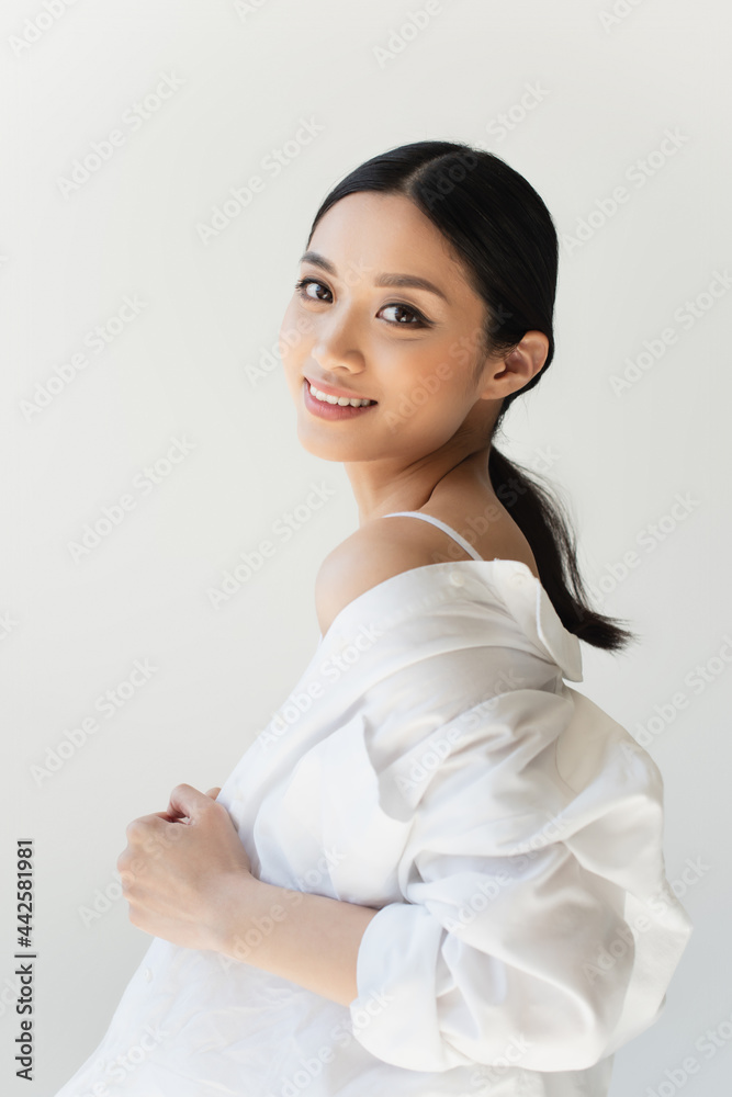 Pretty asian woman adjusting white shirt and smiling at camera isolated on grey Pretty asian woman adjusting white shirt and smiling at camera isolated on grey
