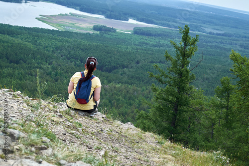 The girl sits on the edge of the mountain with her back. Looks into the distance at Lake Sugomak in the Chelyabinsk region. Trekking and walks in the Urals. Looks thoughtfully into the distance. photo