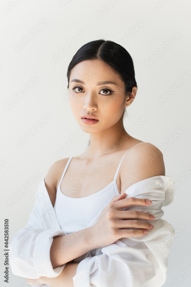Young asian woman in white clothes touching arm isolated on grey Young asian woman in white clothes touching arm isolated on grey