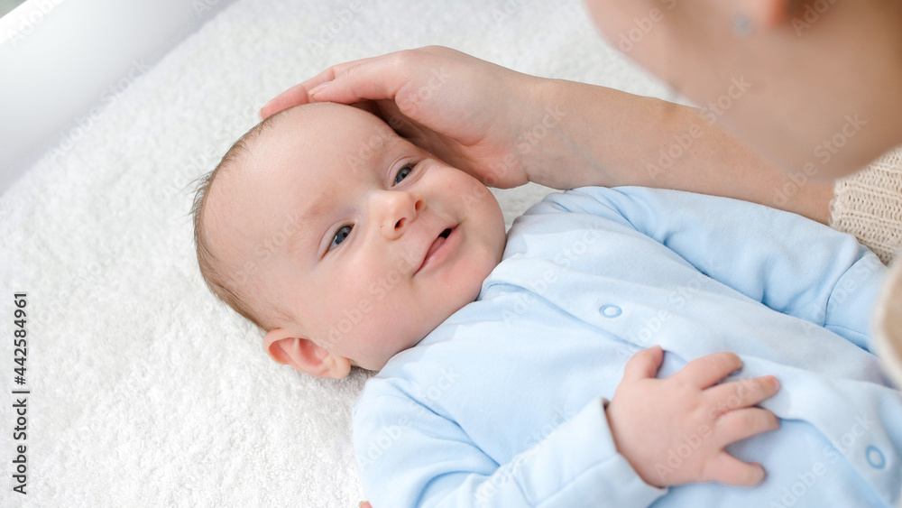 Adorable baby boy smiling at mother while she is stroking him on dressing table. Concept of hygiene, baby care and healthcare Adorable baby boy smiling at mother while she is stroking him on dressing table. Concept of hygiene, baby care and healthcare