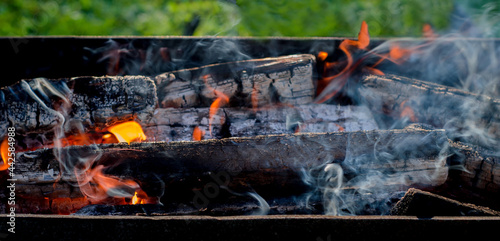 Burning wood in a barbecue grill. Open fire, flames, smoke from burning firewood in nature